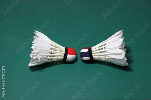 Two used shuttlecocks on green floor of Badminton court with both head each other. One head painted with Indonesia flag And one head painted with the Thai flag. photo