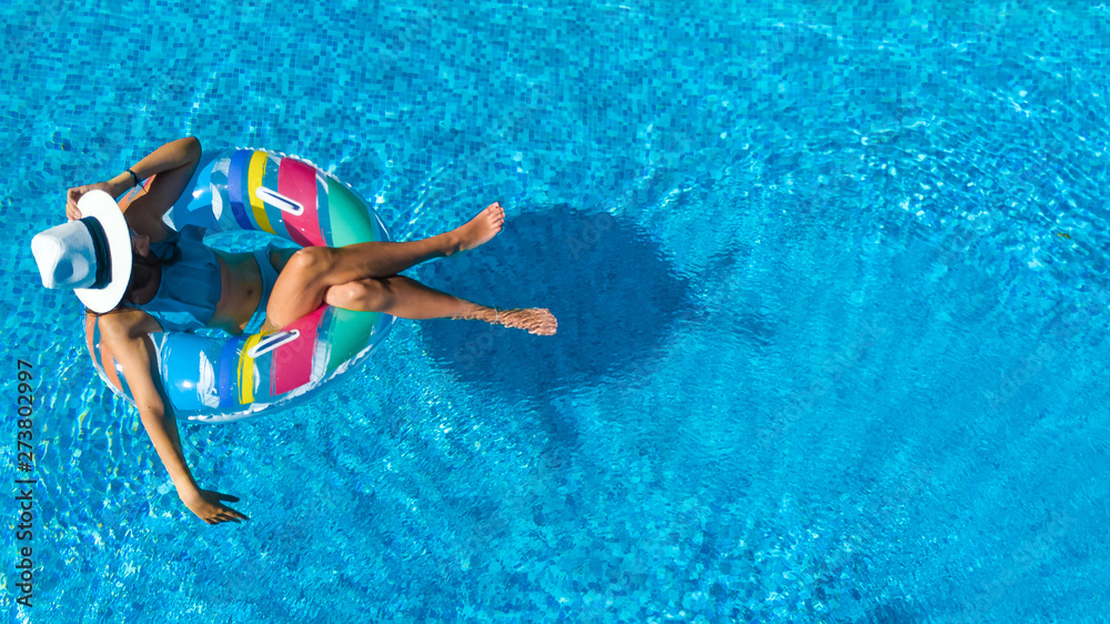 Beautiful girl in hat in swimming pool aerial top view from above, young woman relaxes and swims on inflatable ring donut and has fun in water on family vacation, tropical holiday resort