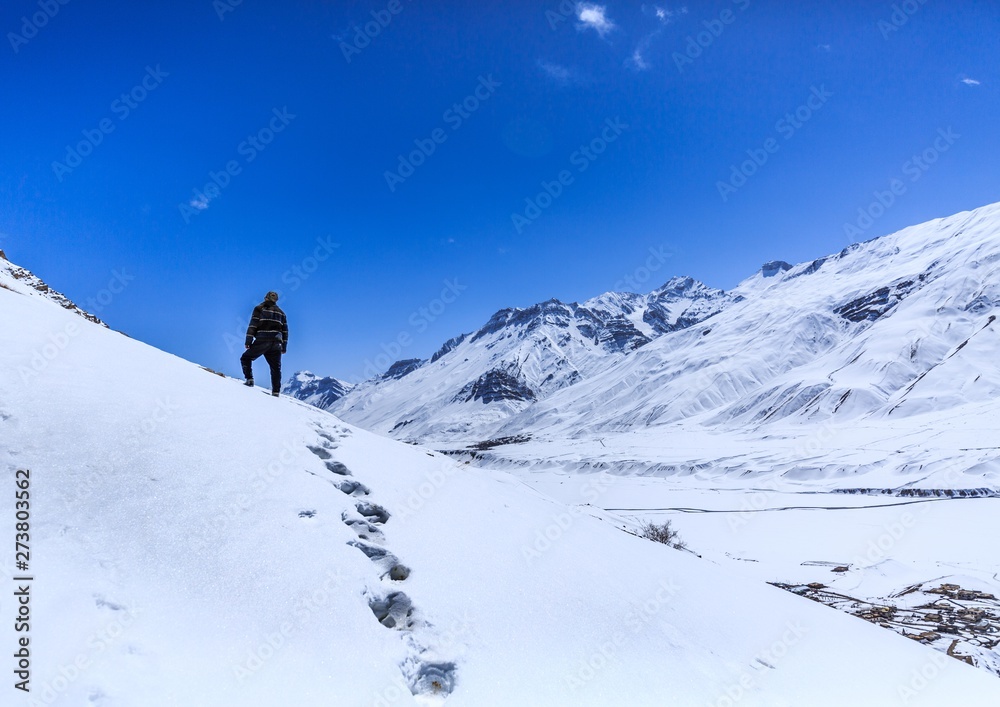 wanderlust trekker standing on top of a mountain surrounded by snow in winter in the Himalayas, seeking for more
