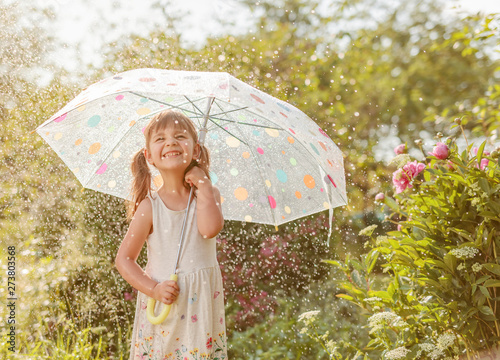 Cuadro en lienzo Happy little girl in garden under the summer rain with an umbrella