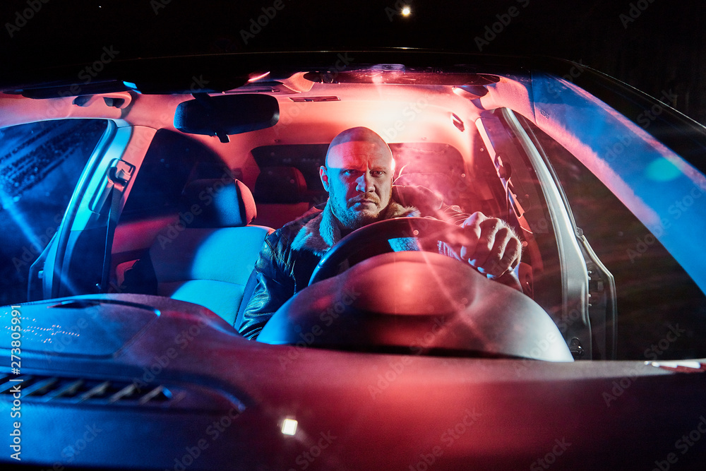 Fototapeta premium Male driver in a leather jacket in the car in the dark. Night photo shoot