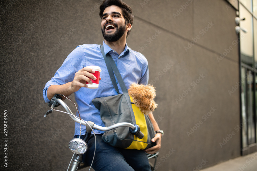 Handsome young man sitting on bike and holding coffee cup on street