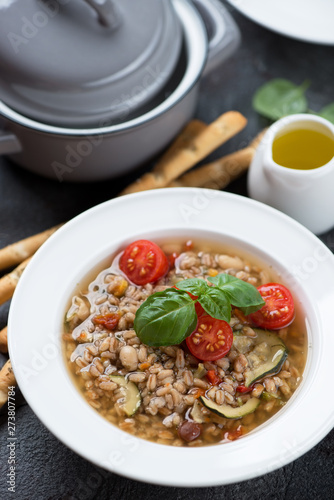 Italian spelt and minestrone soup topped with cherry tomatoes and fresh green basil, vertical shot