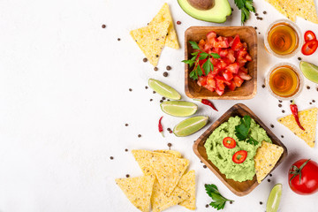 Mexican food selection: sauce guacamole, salsa, chips and tequila shots with lime on white background