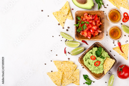 Mexican food selection: sauce guacamole, salsa, chips and tequila shots with lime on white background