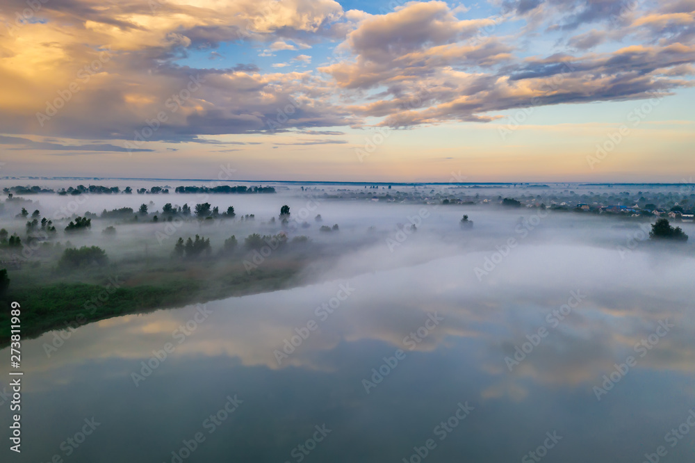Forest lake in the morning fog, in the rays of the dawn sun. Drone view.