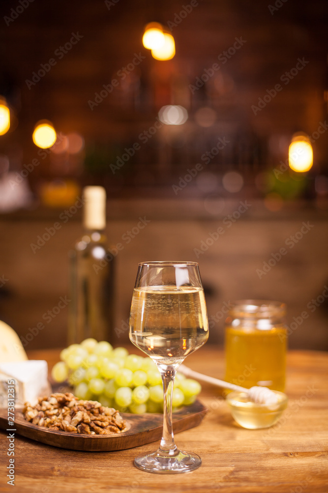 Rafined still life of wine, grapes,different cheeses over rustic wooden table in a vintage pub