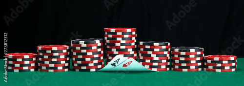 on a green table, for playing poker, pyramids of chips of different colors and two raised cards, aces, on top of a black background for the inscription