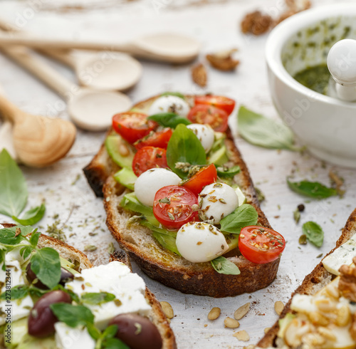 Open sandwiches, in the middle of board an open avocado sandwich made of slice of sourdough bread with the addition of cherry tomatoes, mini mozzarella, fresh basil, olive oil and oregano, close-up photo