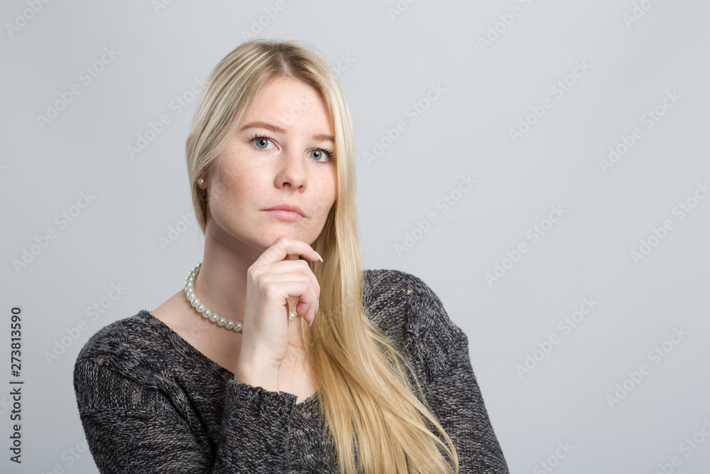 young blonde woman with hand at her chin is thinking young blonde woman with hand at her chin is thinking