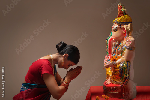 Woman praying with hands joined and eyes closed in front of Ganpati Idol.	 photo
