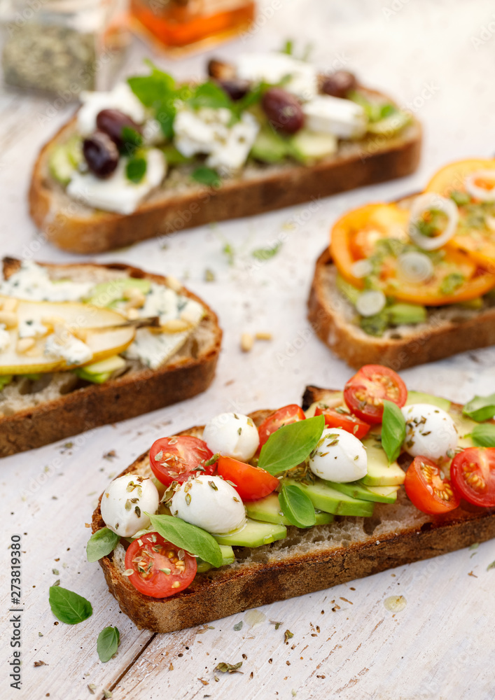 Assorted open faced sandwiches, Open avocado sandwiches made of slices of sourdough bread with various toppings on a white wooden table, top view. Delicious and nutritious breakfast Assorted open faced sandwiches, Open avocado sandwiches made of slices of sourdough bread with various toppings on a white wooden table, top view. Delicious and nutritious breakfast