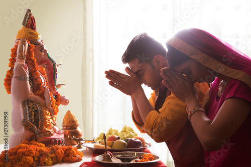 Husband and wife praying with hands joined in front of Ganesha Idol on the occasion of Ganesh Chaturthi	 photo