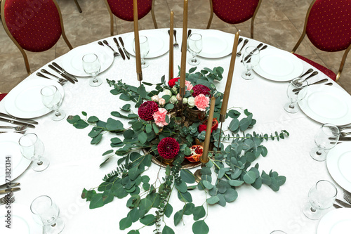 The wedding table setting is decorated with fresh flowers in a brass bowl and golden candles in brass candlesticks. Wedding floristry. Banquet table for guests. Bouquet with dahlias and eucalyptus