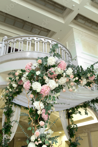 Beautiful wedding huppah decorated with fresh fresh flowers from hydrangea and eucalyptus sheets in a large beautiful wedding hall with a balcony. Wedding floristry