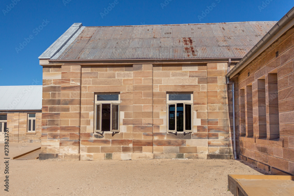 Sandstone convict brick made building with corrugated iron roof, open windows, pebbled courtyard against blue sky