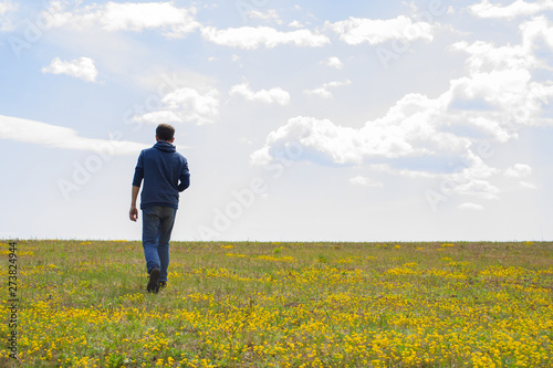 A young man walks across a field of yellow flowers. The concept of freedom, loneliness. Free space for text.
