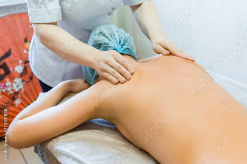 A female masseur does a back massage to a young girl in a Spa salon. The girl lies on the massage table.