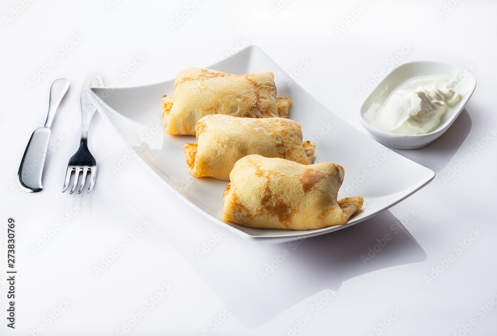 Pancakes with a meat, eggs and onions stuffing. Sour cream. White background. Close up. Selective focus.