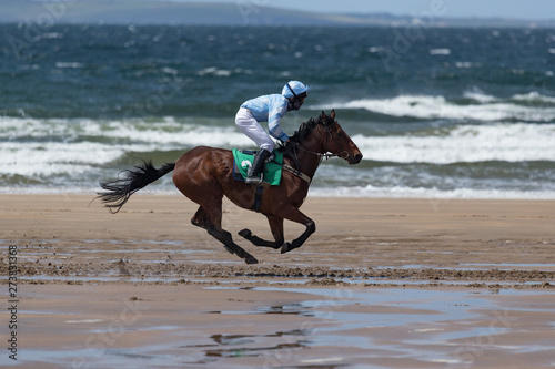 Jockey and race horse galloping on a wet sandy beach