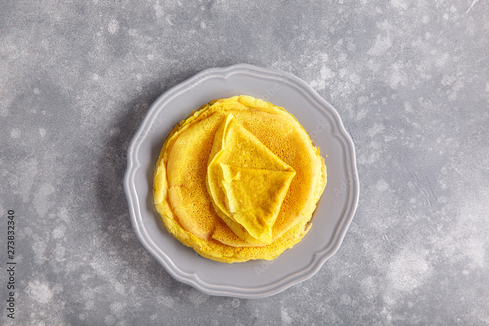 Yellow pancakes on gray plate. Stack of crepes tinted turmeric on concrete background. Top view, copy space. Yellow pancakes on gray plate. Stack of crepes tinted turmeric on concrete background. Top view, copy space.