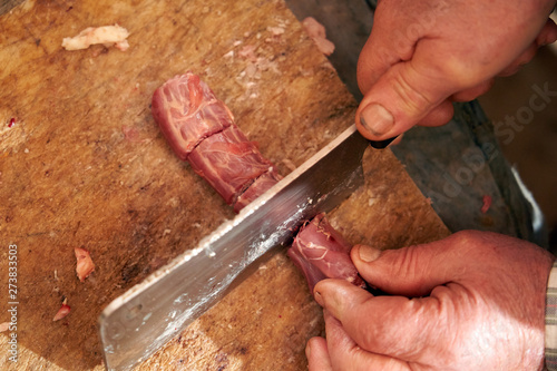 An older man cutting raw meat. Rural. Self-consumption.