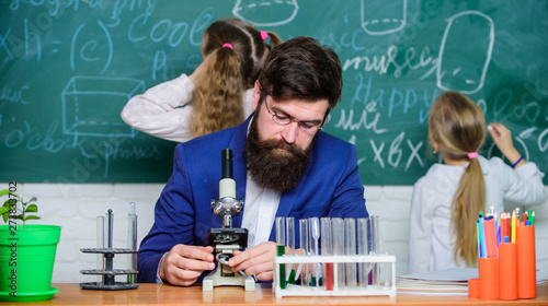 Man bearded teacher work with microscope and test tubes in biology classroom. Explaining biology to children. Biology plays role in understanding of complex forms of life. School teacher of biology
