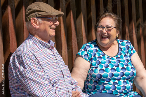 Pareja de gente mayor (abuelos) sentados en un banco descansando del paseo. Se ríen y hablan entre ellos.