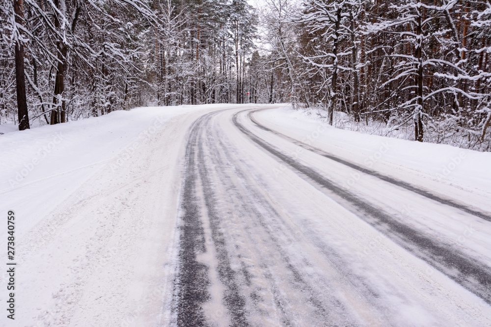 Fototapeta premium Patterns on the winter highway in the form of four straight lines. Snowy road on the background of snow-covered forest. Winter landscape.
