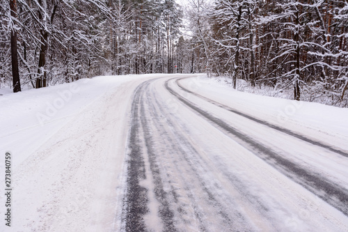 Patterns on the winter highway in the form of four straight lines. Snowy road on the background of snow-covered forest. Winter landscape.