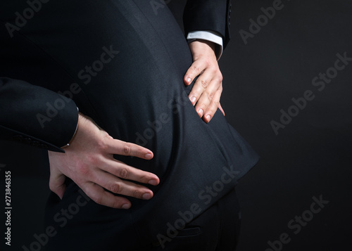Businessman in a suit having a backache. Bending over in pain wi