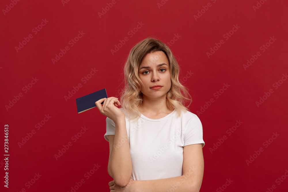 Portrait of a beautiful girl with curly blond hair dressed in a white t-shirt standing on a red background.