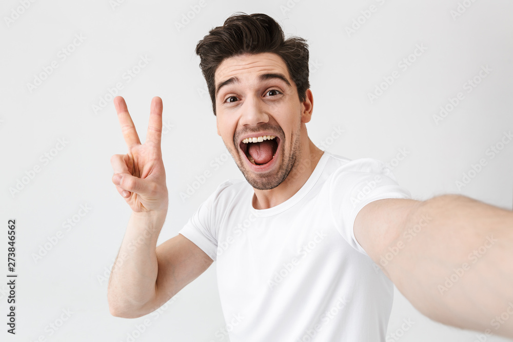 Excited happy young man posing isolated over white wall background make a selfie by camera. Excited happy young man posing isolated over white wall background make a selfie by camera.