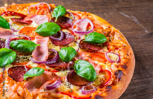 Pizza with Mozzarella cheese, ham, tomato sauce, salami, onion, pepper, Spices and Fresh basil. Italian pizza on wooden table background