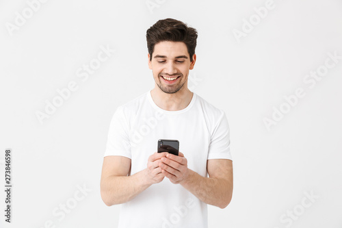 Excited happy young man posing isolated over white wall background using mobile phone. © Drobot Dean