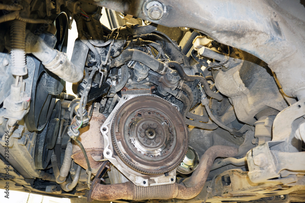 The engine of the modern car during the repair.  Bottom view from the gearbox side when the gearbox is removed. Flywheel, exhaust system,  cooling system, pipes. Car lifted on the lift.