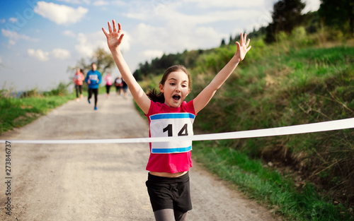 Obraz na plátně Small girl runner crossing finish line in a race competition in nature
