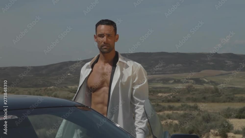 Handsome businessman in white shirt open, feeling freedom, standing and alone in the desert in front of his sports car with mountain in sunny summer. Beautiful abs, fitness model, Medium Shot. Handsome businessman in white shirt open, feeling freedom, standing and alone in the desert in front of his sports car with mountain in sunny summer. Beautiful abs, fitness model, Medium Shot.