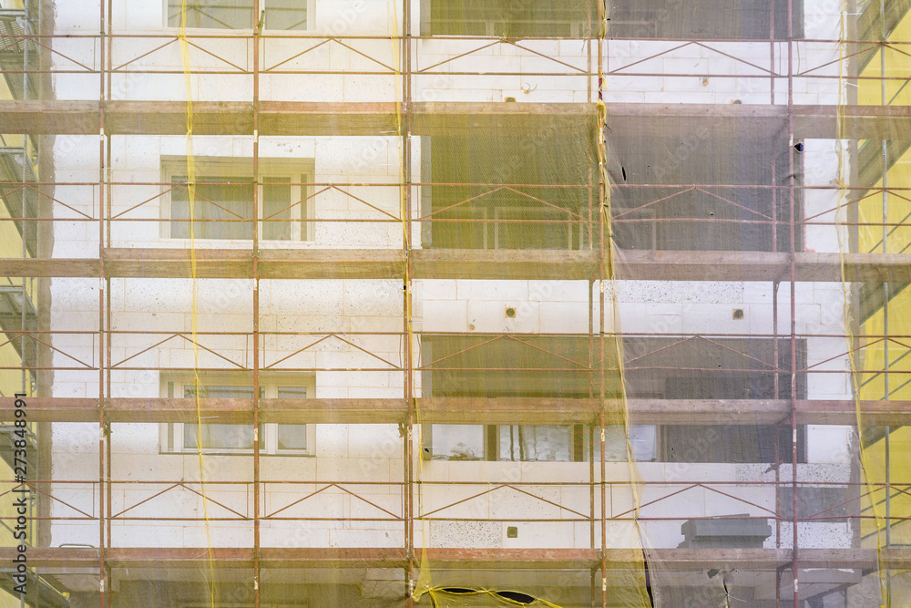 Obraz premium Building facade renovation, old house reconstruction, repair. Scaffold in front of building facade covered with yellow transparent fabric