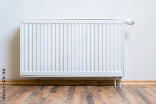 Home radiator heater on the white wall on wooden hardwood floor. Adjustable warming equipment for apartment and home photo
