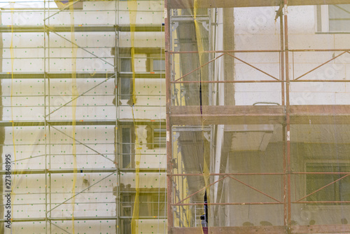 Building facade renovation, house reconstruction, repairBuilding facade renovation, old house reconstruction, repair. Scaffold in front of building facade covered with yellow transparent fabric