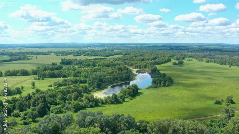Aerial perspective shot.Follow the small lake among the trees and meadows.Beautiful blue sky and white clouds.Blue lake,green grass.Summer day. Aerial perspective shot.Follow the small lake among the trees and meadows.Beautiful blue sky and white clouds.Blue lake,green grass.Summer day.