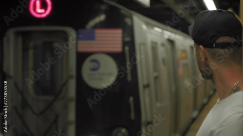 Caucasian man with black cap looking at subway arriving at subway platform in New York City.