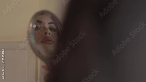Attractive brunette Arab woman holding Old Silver makeup mirror vintage, looking at her reflection in the mirror, touching her lips. Hands in red varnish. Hotel room in Paris with Sun light flare. 