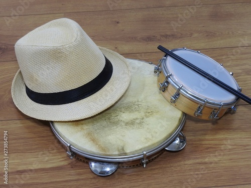 A samba player (sambista) hat and two Brazilian percussion musical instruments: pandeiro (tambourine) and tamborim with drumstick. The instruments are widely used to accompany samba music.