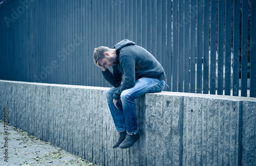 Unhappy depressed caucasian male sitting on urban street feeling photo