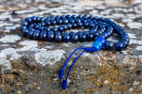 Blue mala beads on stone wall, close up and selective focus. Yoga and meditation accessory. photo