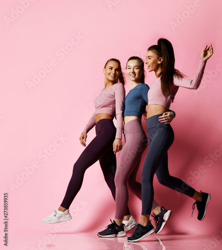 Good shaped sport girls friends in blue, grey, brown Sportwear walk together, talk and laugh. Fitness and yoga girls on pink background
