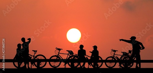 Silhouette group friend and bike relaxing on blurry sunset background.