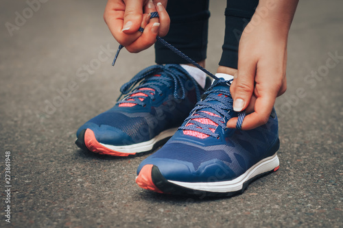 Evening run. Young lady running on a rural road during sunset in blue sneakers. Girl tying shoelaces before running